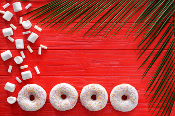 Composition with tasty donuts, palm leaves and place for text on color wooden background