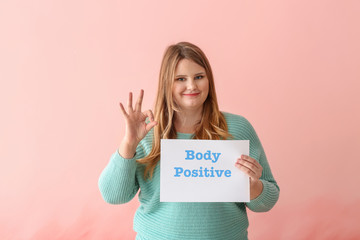 Fototapeta na wymiar Beautiful plus size girl holding paper sheet with text BODY POSITIVE on color background