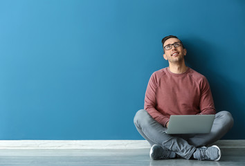Young man with laptop sitting near color wall