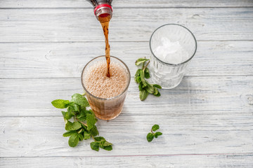 Pouring of tasty cola drink into glass on white wooden table