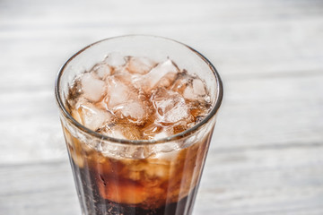 Glass of tasty cold cola drink on white wooden table