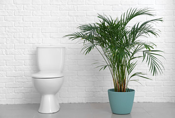 Modern ceramic toilet bowl near white brick wall in restroom
