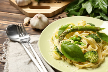 Plate with tasty pasta and green vegetables on wooden table