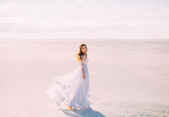 Fototapeta na wymiar A lovely sweet girl in an elegant white dress with transparent sleeves walks on the white sand of the Maldives during her summer vacation and smiles brightly and sweetly. positive sincere emotions