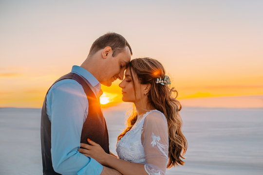 Unusual wedding photo shoot in the desert. Background white sands at sunset. Happy brunette girl with long hair and a guy touch each other. The picture will fill the love and and the rays of the sun