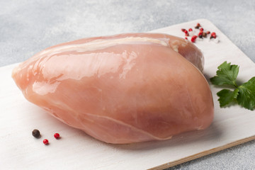 Raw chicken breasts and spices on wooden cutting board, close up view.