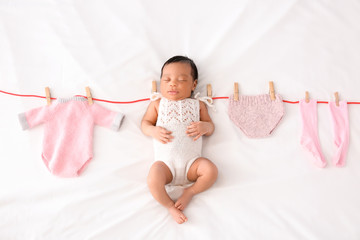 Cute African-American baby with clothes on rope lying on white blanket