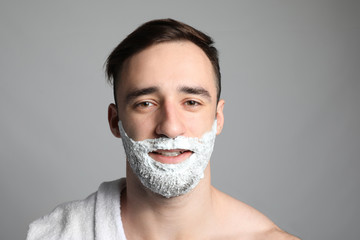Handsome man with shaving foam on his face against grey background