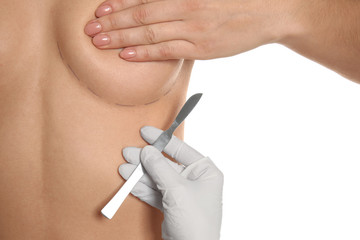 Naked woman and doctor's hand with lancet on white background, closeup. Concept of breast augmentation