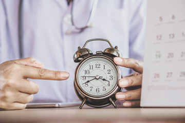 closeup doctor hand holding alarm clock showing the time ,can be used for appointment or over work concept 