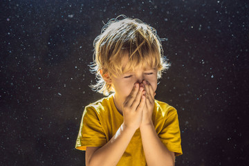 Allergy to dust. Boy sneezes because he is allergic to dust. Dust flies in the air backlit by light