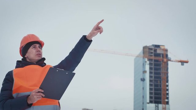 Business, building, paperwork and people concept - happy builder in hardhat with clipboard at construction site. Engineer builders with blueprint at construction site.