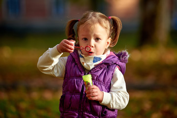 Little girl child enjoying playing with soap bubbles in autumn park