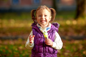 Little girl child enjoying playing with soap bubbles in autumn park