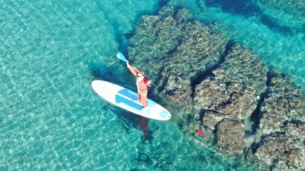 Aerial photo of fit man dressed as Santa Claus practising SUP or Stand Up Paddle in exotic...