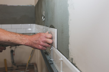 Man is putting white tiles on the grey concrete. Maintenance repair works renovation in the flat....