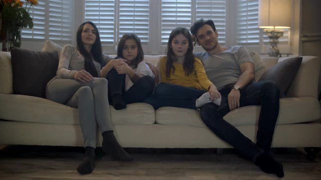 Family watching tv together on the sofa. Slow dolly towards them