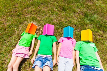 Four kids laying on a ground with books on their faces