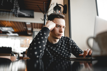 Young guy or freelancer is bored while sitting at a laptop