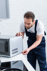 Obraz premium serious adult handyman repairing microwave oven in kitchen