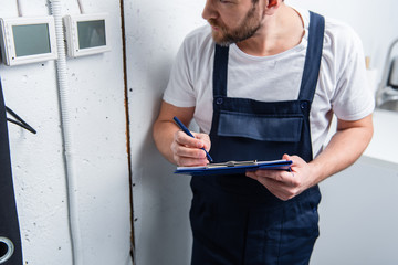 cropped image of adult electrician with clipboard checking electrical panel
