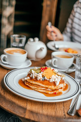 Perfect breakfast in the city cafe with pankakes, oatmeal, coffe and tea on the round wooden table.