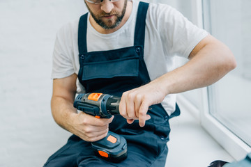 partial view of male handyman with electric drill sitting on windowsill