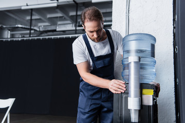 serious handyman in working overall checking broken water cooler