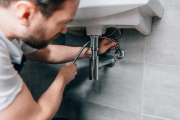 selective focus of male plumber in working overall fixing sink in bathroom - obrazy, fototapety, plakaty