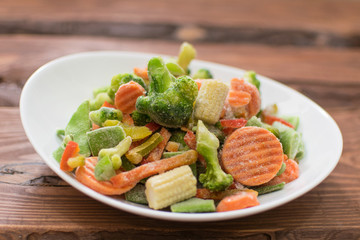 Frozen various vegetables on a plate on a wooden background.