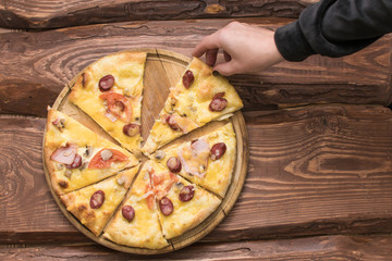 Female hand takes pizza pieces on a dark wooden background.