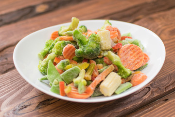 Frozen various vegetables on a plate on a wooden background.