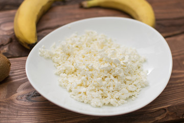 Cottage cheese in a plate on a wooden background.