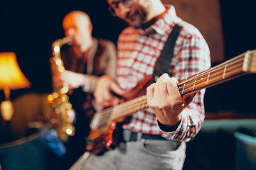Close up of talented bass guitarist playing his instrumet. In background saxophonist playing sax....