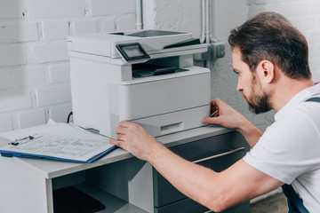 focused male handyman repairing copy machine in modern office