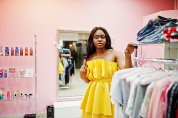 Stylish african american woman at yellow dreess posed at pink shop and chooses clothes.