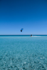 A kitesurf with its sail and the board, cuts the line that divides the blue sky from the crystalline sea of Sardinia