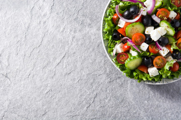 Fresh Greek salad in Plate with black olive,tomato,feta cheese, cucumber and onion on gray background. Top view. Copyspace