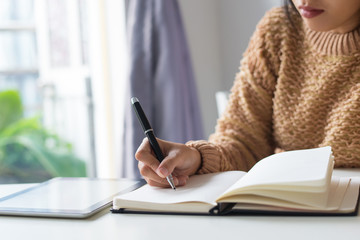 Close-up of pensive woman writing out ideas in diary. Busy woman sitting at table and making notes....