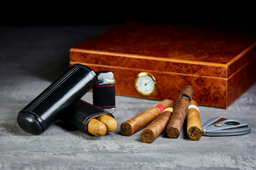 Six Cuban cigars on a stone table with a lighter, cutter and a wooden humidor and leather case.