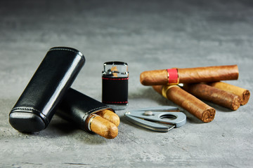 Six Cuban cigars on a stone table with a lighter, cutter and a leather case