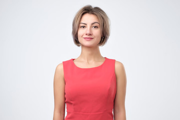 Obraz premium Charismatic attractive caucasian woman in red dress, smiling cheerfully while standing against gray background, posing for id photo