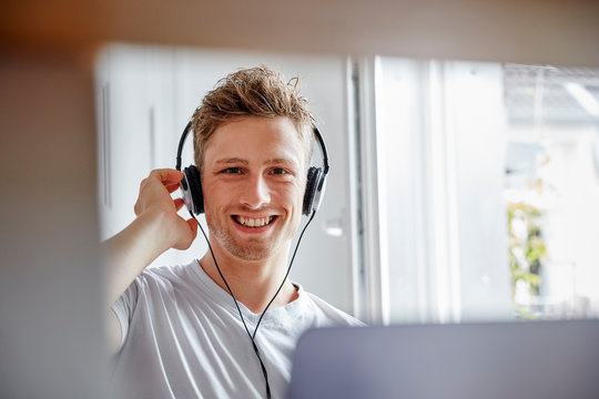 Portrait of smiling young man at home listening to music with headphones
