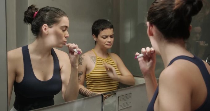 Couple of Female Roomates in The Bathroom Brushing Teeth Together