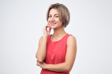 Charismatic attractive caucasian woman in red dress, smiling cheerfully while standing against gray background, posing for id photo