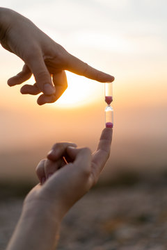 Close-up of man's hands holding an hourglass at sunset