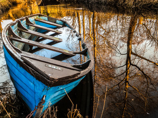 damaged wooden boat in the water with mirrored trees