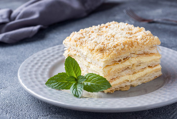 Layered cake with cream Napoleon millefeuille vanilla slice with mint on dark background.