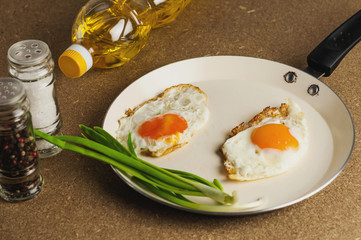 Two fried eggs in metal beige pan near bottle with oil and spices