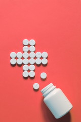 white pills laid out in the shape of a cross. white pills scattered on a pink background. pills spilled out of the bottle. copy space for text
